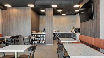 A modern restaurant interior with high tables, chairs, a bar area, and a flat-screen TV mounted on the wall.