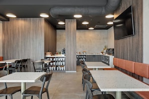 Ein modernes Restaurantambiente mit hohen Tischen, Stühlen, einer Bar und einem an der Wand befestigten Flachbildfernseher.