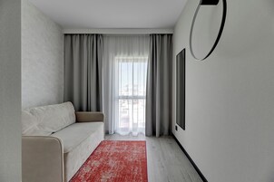 A modern living room with a sofa, a red rug, a large window with curtains, and a mounted TV.
