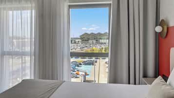 A hotel room with a large bed, a view of a parking lot, and a building with a modern design.