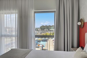 A hotel room with a large bed, a view of a parking lot, and a building with a modern design.