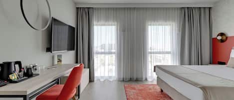 A hotel room with a bed, a desk with a chair, a TV, and a window with curtains.