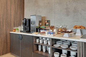 Un bar de desayuno autoservicio con máquinas de café, diversas opciones de comida y una selección de pasteles.