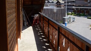 A wooden balcony with a view of a mountainous landscape, a covered walkway, and a parking area.