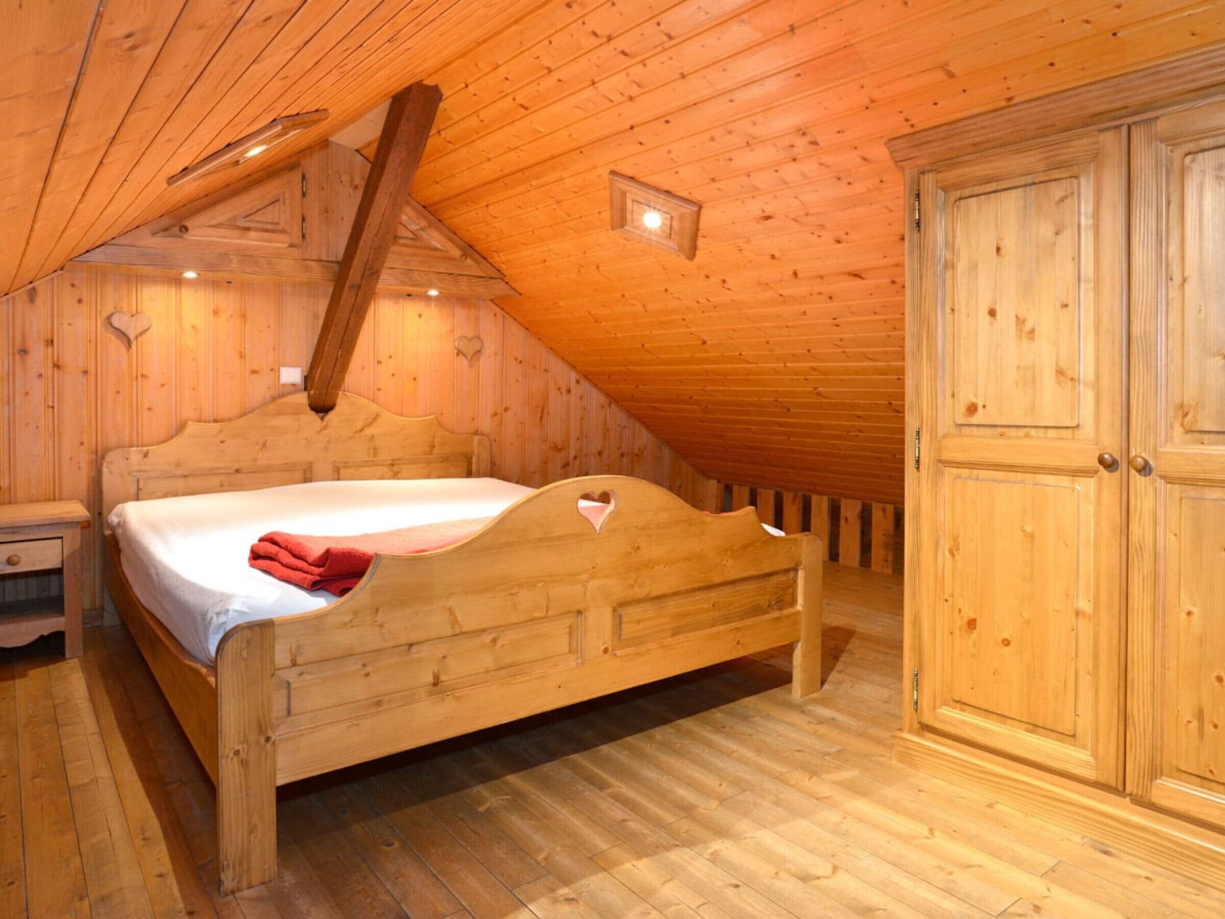 A wooden bedroom with a sloped ceiling, a single bed, a nightstand, and a wardrobe.