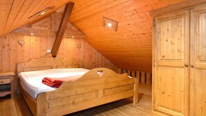 A wooden bedroom with a sloped ceiling, a single bed, a nightstand, and a wardrobe.