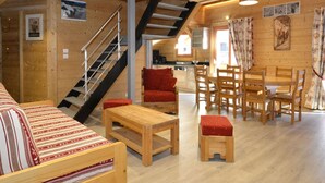 A cozy cabin interior with a wooden staircase, a dining area, and a living room with a sofa and a small table.