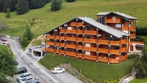 Een hotel met meerdere verdiepingen en balkons, gelegen in een glooiend, groen gebied met een parkeerplaats en een weg in de buurt.