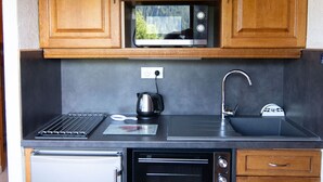 Een keuken met houten kastjes, een magnetron, een waterkoker, een broodrooster en een spoelbak.