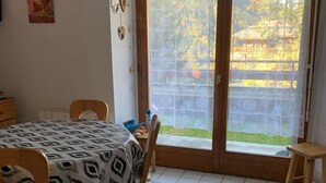 A room with a dining table, chairs, a bed, and a sliding glass door leading to a garden. - Charming 2-Room Apartment, Sleeps 5, Terrace, Parking, Pet-Friendly (Châtel)