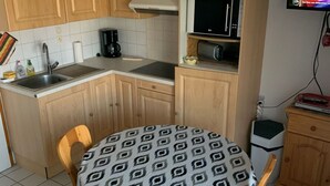 A compact kitchen with wooden cabinets, a microwave, a coffee maker, and a small table with a patterned tablecloth. - Charming 2-Room Apartment, Sleeps 5, Terrace, Parking, Pet-Friendly (Châtel)