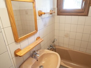 Un baño con un lavabo color beige, un espejo con marco de madera, una bañera y una ventana sobre el lavabo.