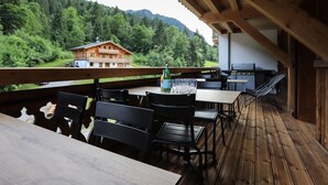 An outdoor wooden deck with tables and chairs, overlooking a forested mountain area. - Large 7-room chalet, 15 people, sauna, jacuzzi in Châtel (Châtel)