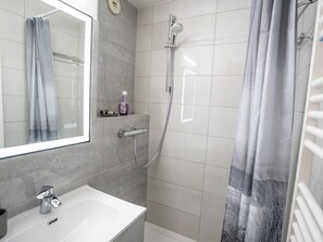 A modern bathroom with a white sink, a mirror, a shower with a handheld showerhead, and a grey shower curtain.