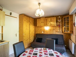 A cozy room with wooden walls, a sofa, a dining table with a patterned tablecloth, and a chandelier.