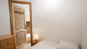 Un dormitorio con un armario de madera, una mesita de noche con lámpara y una cama con ropa de cama blanca.