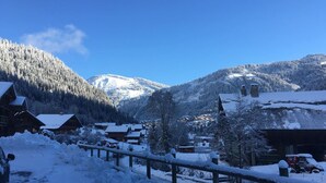 Un pueblo cubierto de nieve en las montañas, con edificios de madera, cielo azul despejado y un sendero nevado.