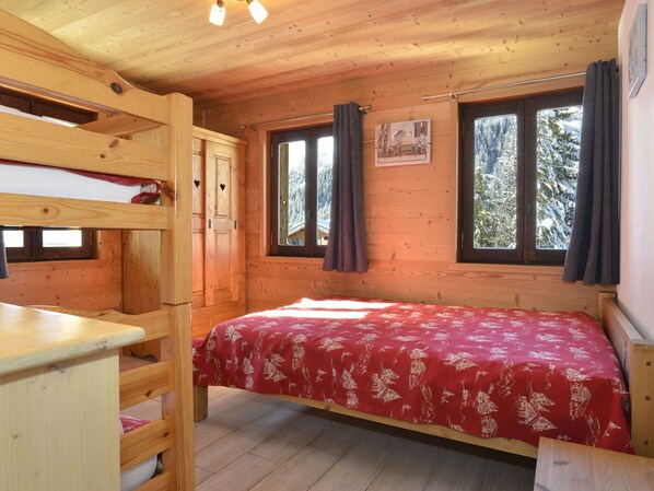 A wooden cabin room with a bunk bed, a small table, and two windows with curtains.