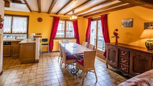 Un rincón acogedor para comer con una mesa y sillas de madera, una cocina con armarios de madera y vistas al exterior a través de amplias ventanas con cortinas rojas.