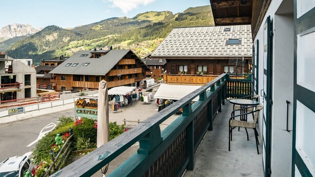 Un balcón con vistas a edificios tradicionales de madera, un cartel que indica 'La Grosse' y montañas al fondo.