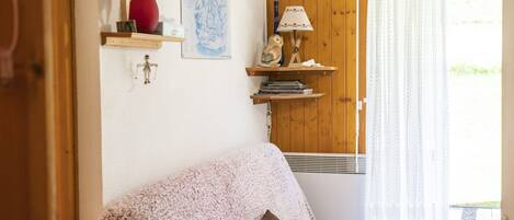 A cozy living room with a wooden door, a red vase, a map, and a lamp on a shelf.