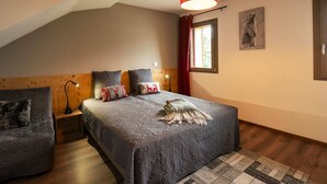 A bedroom with a sloped ceiling, a bed with a patterned bedspread, two bedside tables with lamps, a window with red curtains, and a painting on the wall. - Spacious 4-room apartment for 7 people, terrace, garage (Châtel)