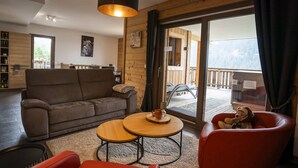 A cozy living room with a sofa, a red chair, and a wooden coffee table. - Spacious 4-room apartment for 7 people, terrace, garage (Châtel)
