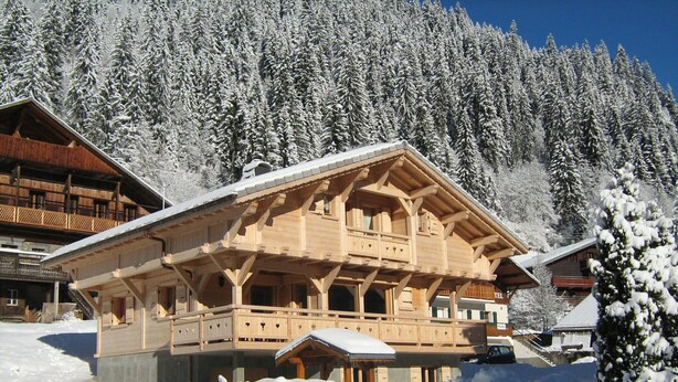 Een houten chalet met balkon, omgeven door sneeuwtakken.