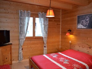 A wooden room with a bed, curtains, a television, and a wall-mounted lamp.