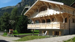 Een houten chalet met een balkon, met daags achterover een berglandschap.