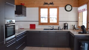 Een moderne keuken met een centraal eiland, roestvrijstalen apparatuur en een houten plafond.