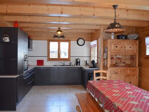 A kitchen with wooden cabinets, a refrigerator, a sink, and a dining table with a red tablecloth.