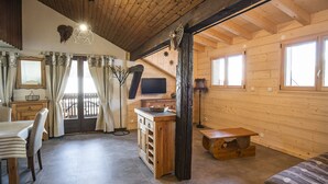 L’intérieur chaleureux d’un chalet comprend un plafond en bois, un coin repas avec une table et des chaises, un coin cuisine avec un évier et des placards, et un espace de vie avec un canapé.