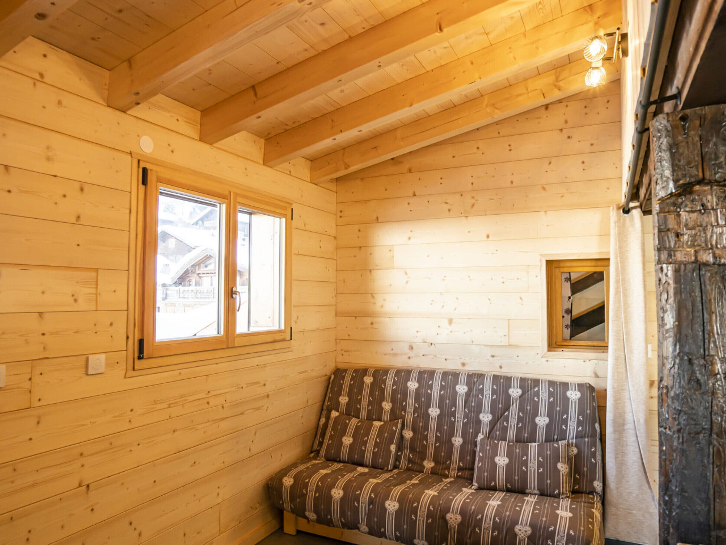 A wooden cabin interior with a sofa, a window, and a stone fireplace.