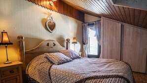 Une chambre confortable avec une tête de lit en bois, une literie à motifs, une décoration murale en forme de cœur et une fenêtre avec des rideaux.