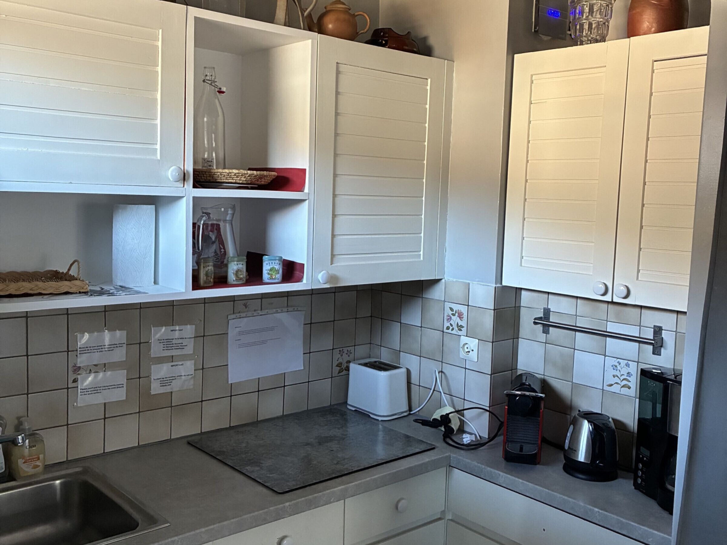 A kitchen with white cabinets, a stainless steel sink, a toaster, a kettle, and a coffee maker.