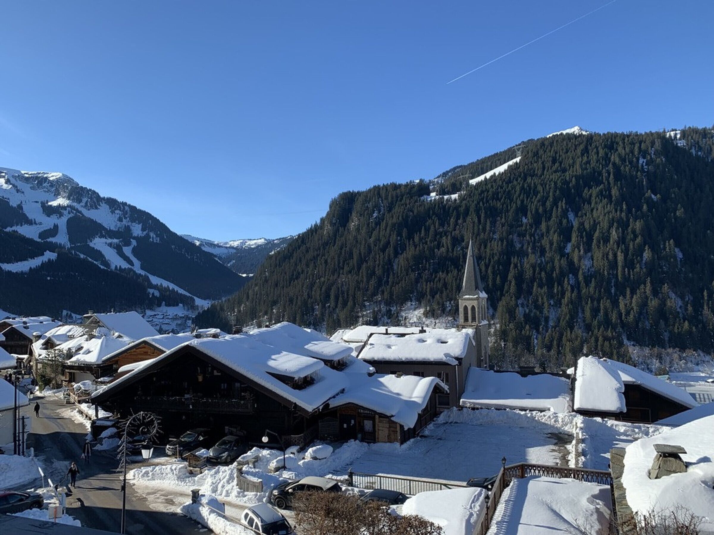 A snow-covered village with wooden buildings, a church, and mountains in the background.