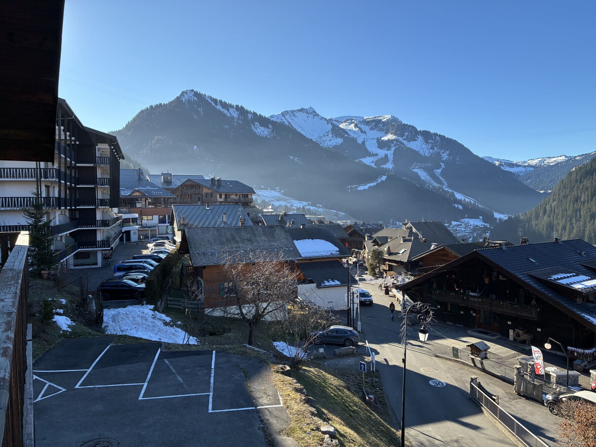 Un pueblo de montaña con edificios, un estacionamiento y montañas nevadas al fondo.