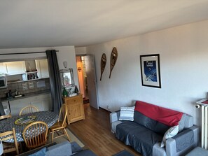 A living room with a sofa, a dining table with chairs, a kitchen area, and a framed picture on the wall.