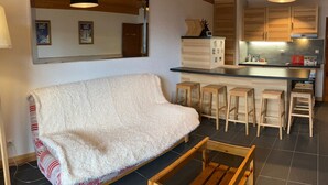 A cozy living area with a sofa, wooden stools, a kitchen with wooden cabinets, and a large mirror.