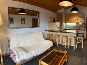 Uma sala de estar aconchegante com sofá, banquinhos de madeira, cozinha com armários de madeira e um espelho grande.