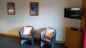 A room with two armchairs, a television, and two posters on the wall.