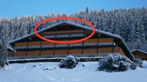 A log cabin with a sloped roof, surrounded by snow-covered trees.