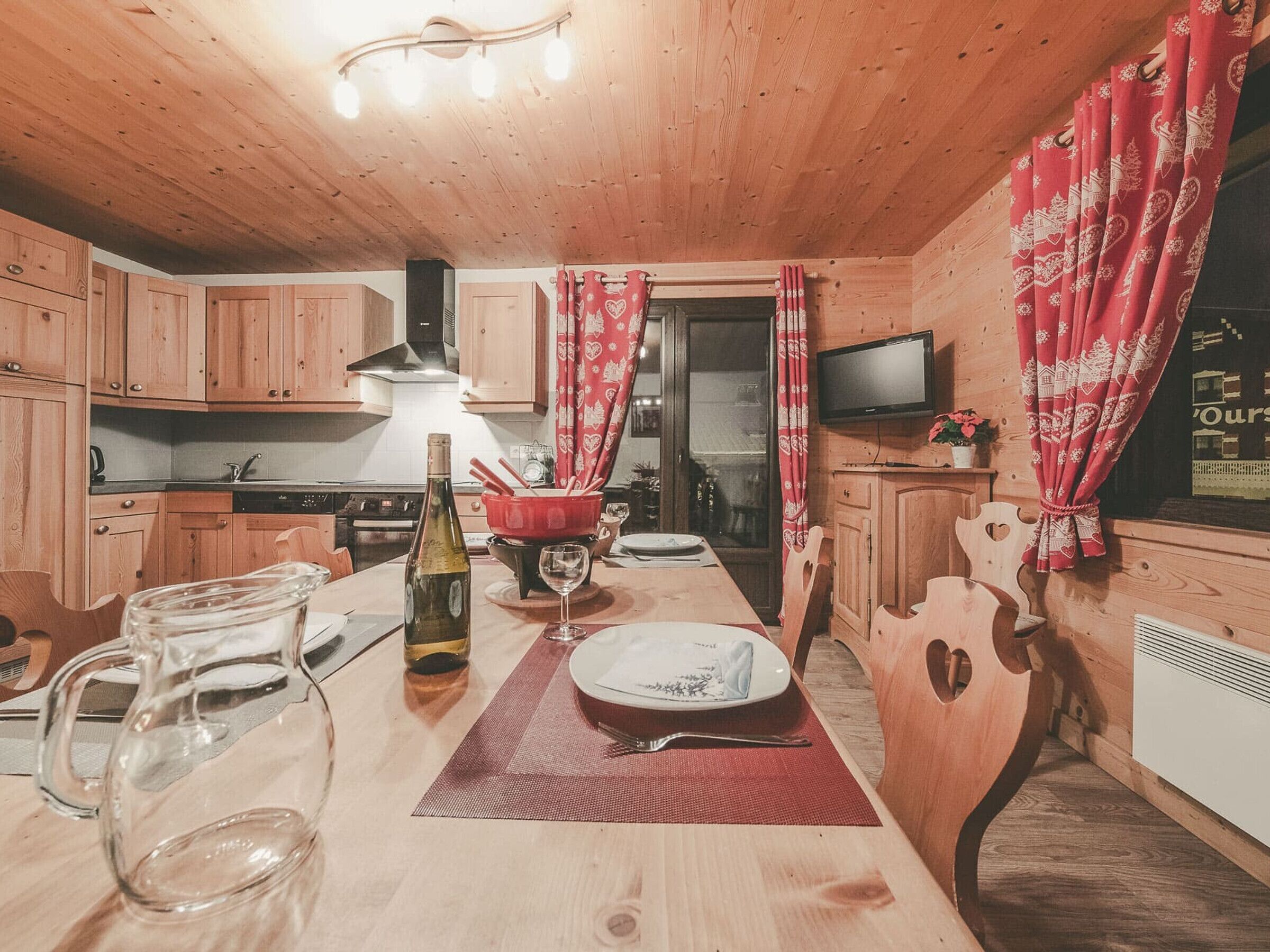 A wooden cabin interior with a kitchen, dining area, and a TV.