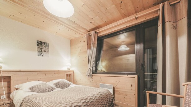 Een knus houten vertrek met een bed, een stoel en een raam met gordijnen.