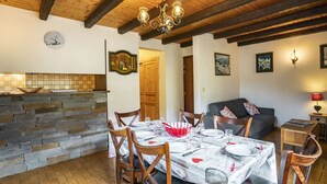A dining area with a stone wall, wooden ceiling beams, a chandelier, and a dining table set for four.