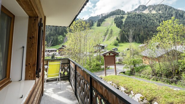 A balcony with a view of a mountainous landscape, a wooden railing, and a yellow chair.