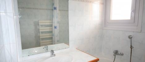 A bathroom with a white sink, a mirror, a wooden cabinet, a bathtub, and a window.