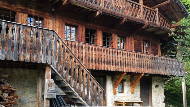 Ein rustikales Holzhäuschen mit Balkon, Steinmauer und Picknicktisch davor.