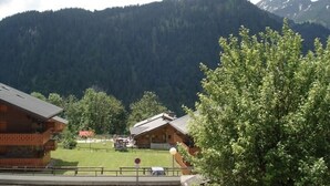 Een bergchalet met houten gevel, een zichtbare garage en een helder uitzicht op het omliggende bos en de bergen.
